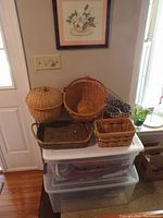 Photo showing six various baskets of different shapes and sizes stacked on plastic drawers by a door and window.