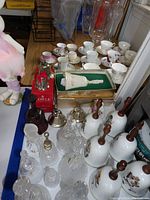Large assortment of bells, cups, and decorative items on a table, featuring various materials like glass, metal, and ceramic.