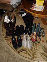 Photo of assorted women's boots and shoes on a patterned carpet floor near a round wooden table.