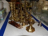Front view of multiple brass candlesticks on a white surface with some used candles and small brass accessories visible in front.