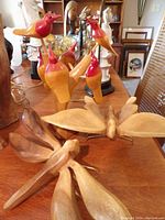 Photo showing a collection of wooden handcrafted birds in red and orange paint, and natural wood-finished butterflies and birds on a wooden table.