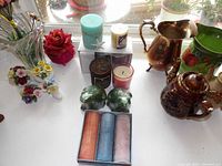 Overview of lot showing multiple candles including a red rose-shaped candle, two green frog-shaped candles, pillar candles in box, and other items on windowsill.