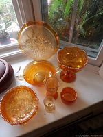 Six pieces of gold carnival glass placed on a windowsill, showing various shapes including bowls, plates, and cups, all with a shiny golden iridescent finish.