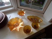 Five gold carnival glass decorative bowls on a windowsill illustrating iridescent gold and orange hues with various edge and pattern designs.