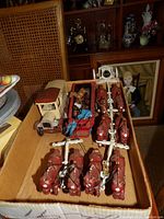 Box of cast iron red horses harnessed in pairs to wagons and a vintage farm truck along with small cast iron animals and barrels.