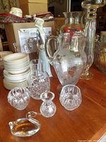 Multiple crystal and glassware items including etched vase, pitchers, votive holders, and decorative figurines.