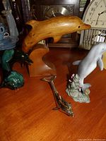Photo showing large wooden dolphin figurine, white resin dolphin, resin sea horse with coral and small dolphin, ceramic dolphin, and metal dolphin bottle opener arranged on wooden surface.