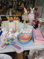 Wide view of table showing grouping of Easter decor items including plush bunnies, ceramic bowls, ceramic bunnies, letter block signs, and cloth napkins