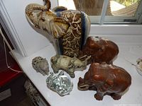 Seven elephant figurines arranged on a windowsill, showing variety in size and material.