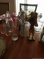Photo showing the three tall figurines on a wooden table surrounded by glassware and chairs in the background.