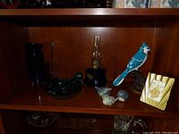 Shelf with a blue glass duck in a bowl, blue Jay figurine, blue lantern, smaller bird figurines, and a striped container