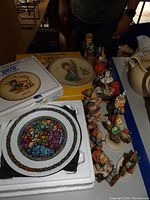 Photo showing M.J. Hummel collectible plates with original boxes including 1971 and 1979 editions, stained-glass style nativity plate, and arranged Goebel figurines.
