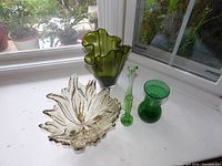 Various green glassware items placed on a white surface by a window, showing the full set of vases and bowl.