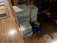 Photo of six Harbour Lights lighthouse collectibles, five in boxes and one unboxed model with red roof cottage on hardwood floor.