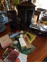 Photo showing hair care products in black packaging, makeup items including a lipstick palette, skincare jars and bottles, and hair scarfs spread on a table.