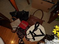 Seven assorted handbags and backpacks arranged on floor under table, showing variety and material.