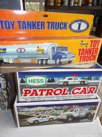 Front view of three boxed trucks: Sunoco Toy Tanker Truck, Hess Patrol Car, and a larger Hess truck with trailer.