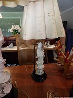 Close-up of one Asian-style table lamp showing carved white figure on black base and scalloped lampshade with floral cutouts.