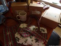 Photo showing three holiday-themed fabric bags, Longaberger pottery coffee mug, and three boxed pottery dishes on table