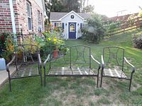 Outdoor set of metal love seat and two metal chairs with armrests, decorative backs, and lattice seats, placed on grass in backyard with a garden shed in the background.