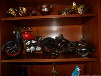 Two metal motorcycle models on wooden shelf—one red and one brown wood finish
