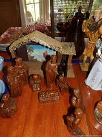 Image showing the full nativity set including the wooden stable with thatched roof and backdrop, and multiple wooden figurines in front representing Mary, Joseph, baby Jesus in a manger, and other nativity characters.
