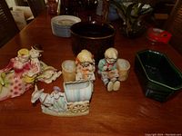 Table display featuring multiple planters and vintage-style ceramic figurines of people and animals.