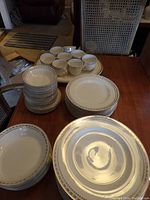 Photo showing stacks of plates, cups arranged on top of a large porcelain tray with gold and beige border design.