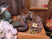 Photo showing three stone garden statues on wooden surface surrounded by artificial flowers, including a duck head and two sets of birds statues.