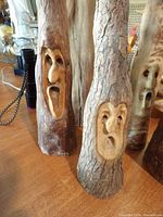 Front angle showing two tree gnomes with carved faces, natural bark texture and detailed expressions.