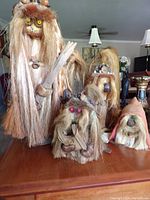 Group photo showing all 5 handmade troll figurines on wooden table with lamp and decorative items in background