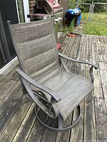 Photo of one brown metal patio rocker chair with mesh fabric seating on wooden deck with grill in background.