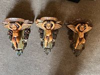 Top-down view of three carved angel wall sconces showing detailed carving, wings, and shelf tops