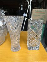 Photo showing two tall crystal vases with diamond cut-glass patterns on a wooden surface in a garage setting.