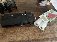 Photo of FoodSaver V2244 vacuum sealer with power cord and box containing rolls of vacuum sealer bags on wooden table.