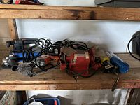 Shelved view showing multiple power tools including angle grinder, drill, and bench grinder placed on wooden shelves