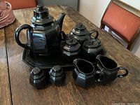 Collection of Mikasa Black China tea set items arranged on wooden table including large and small tea pots, platter, creamers, sugar bowls, and salt & pepper shakers.