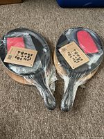 Two sets of small cast iron pans on wooden bases, wrapped in original plastic with red oven mitts on top