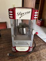 Front view of the red and silver popcorn machine showing the front door with 'Popcorn' script and interior metal kettle with stirring arm.