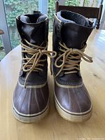 Front view of dark brown Sorel boots laced up, showing waterproof lower rubber section and leather upper.