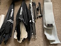 Photo showing multiple folded black softboxes and umbrellas with stands and a grey padded carrying case with Yohann logo.