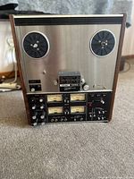 Front view showing two empty reel spindles on top, center tape transport block labeled TEAC 3340, lower control panel with VU meters and control knobs