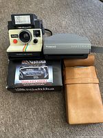 Group shot of Nishika in box, Polaroid OneStep, Spectra 2 and leather case