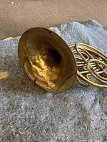 Full view of the French horn showing the flared bell and part of the coiled tubing, highlighting wear and tarnish on brass.