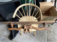 Wooden wall shelf resting on a wooden chair with a carved bow/ribbon detail in front.