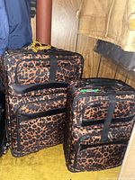 Two leopard print soft-sided luggage pieces standing upright on yellow carpet beside a wooden wall.