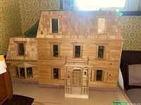 Front exterior view of the three-story wooden dollhouse on its rolling table, showing facade, windows, porch and cedar shingle roof