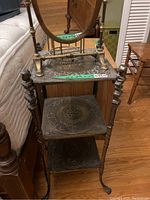 Full view of the antique brass side table with three decorative metal shelves and wooden oval mirror at the top.