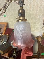 Close-up of the scalloped glass fixture with pink gradient and embossed floral design and brass mount.