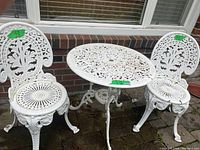 Full view of white cast iron bistro table and two chairs against brick background